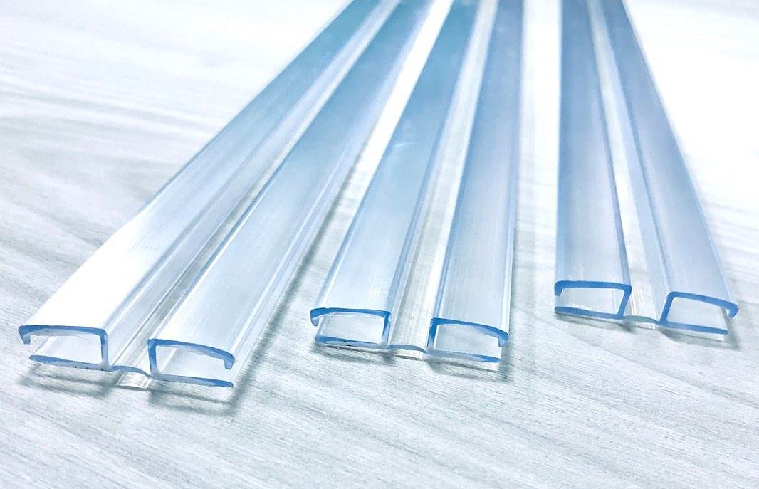 Clear PVC living hinges lying on a pale wood surface