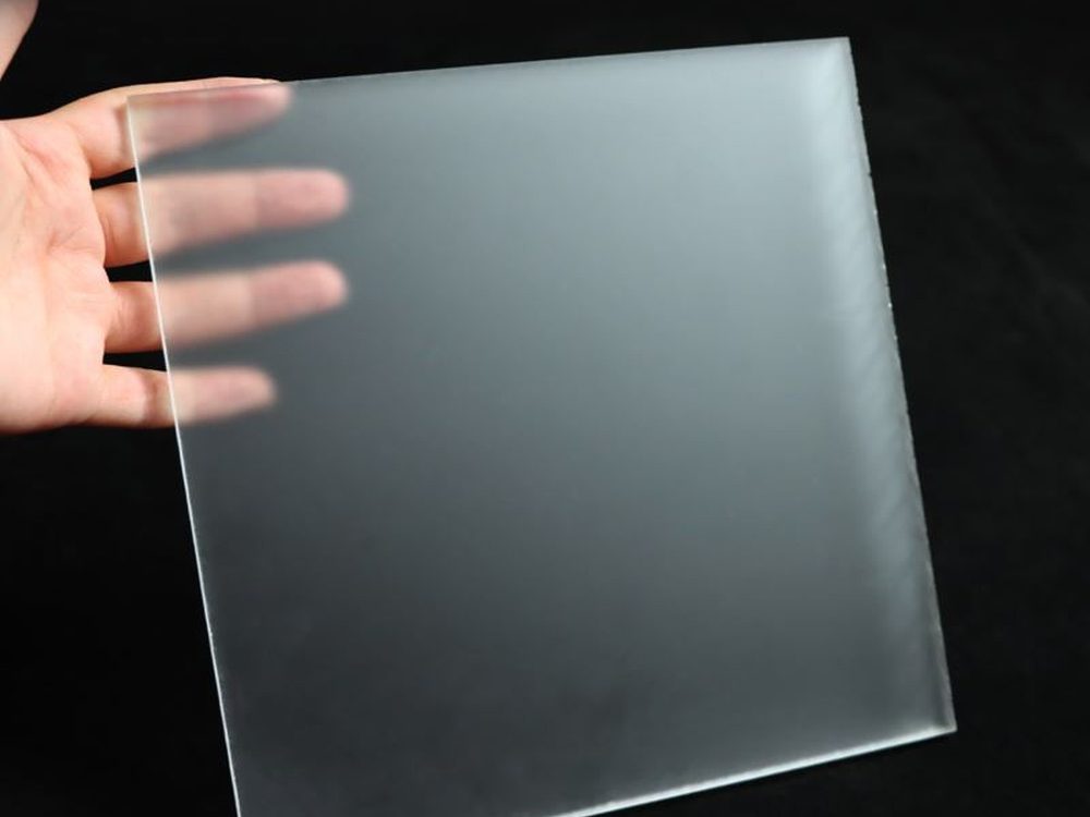 A hand holding a frosted acrylic sheet against a dark background
