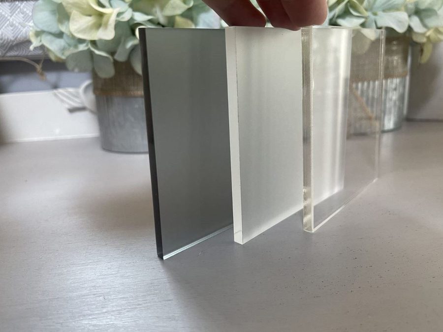 Three acrylic sheets standing side by side, left to right: grey frosted, frosted and clear