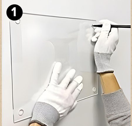 Gloved hands holding an acrylic panel against a wall and marking a hole with a pencil