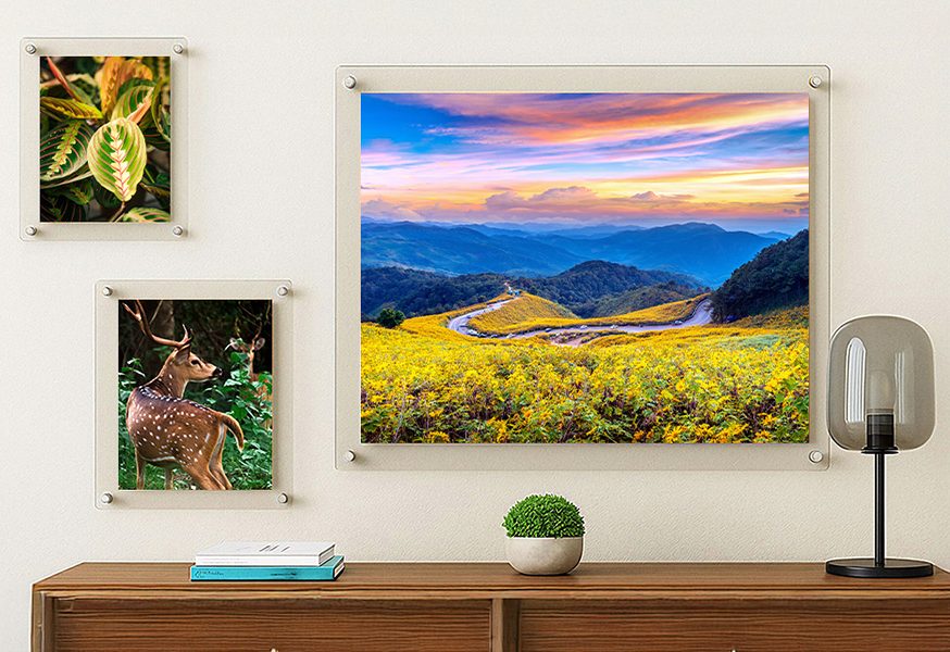 Three clear acrylic floating frames on a wall above a sideboard, the largest holding a mountain landscape