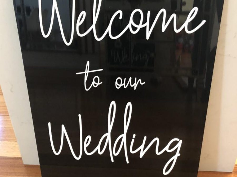 A black acrylic wedding welcome sign with white lettering
