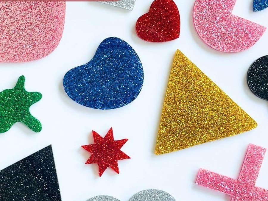 Laser-cut glitter acrylic shapes in pink, gold, silver, red, blue, green and black on a white table